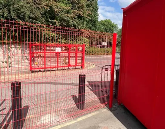 Security Fencing featuring red mesh panels with a matching entrance gate and safety bollards.