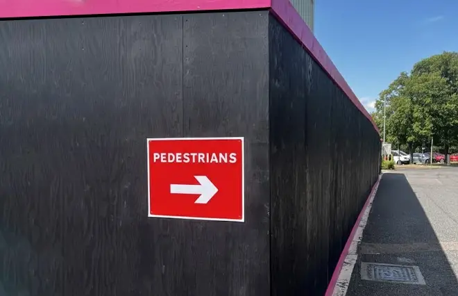 Site Hoarding featuring black wooden security hoarding with magenta trim and a red pedestrian directional sign.