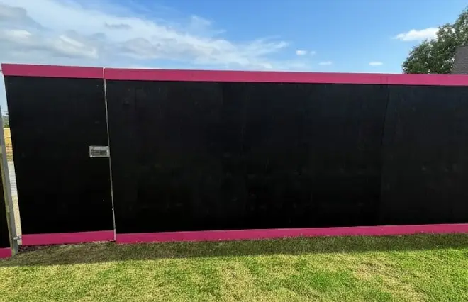 Site Hoarding featuring black wooden security hoarding panels with magenta trim and an access door.