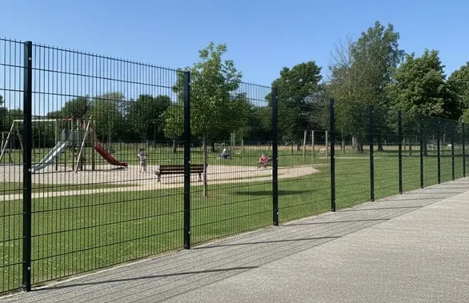 Sports Ground Fencing featuring black rigid wire mesh panels surrounding a children's playground and park area.