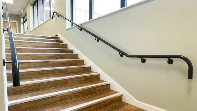 Handrails & Railings featuring wall-mounted dark metal handrails with D-return ends along an indoor staircase.
